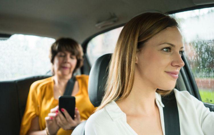 A passenger sits in the back of a car while the driver looks ahead