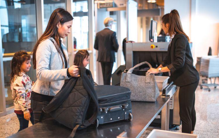 A woman placing her bags on the TSA scanner conveyor belt, with two small kids behind her